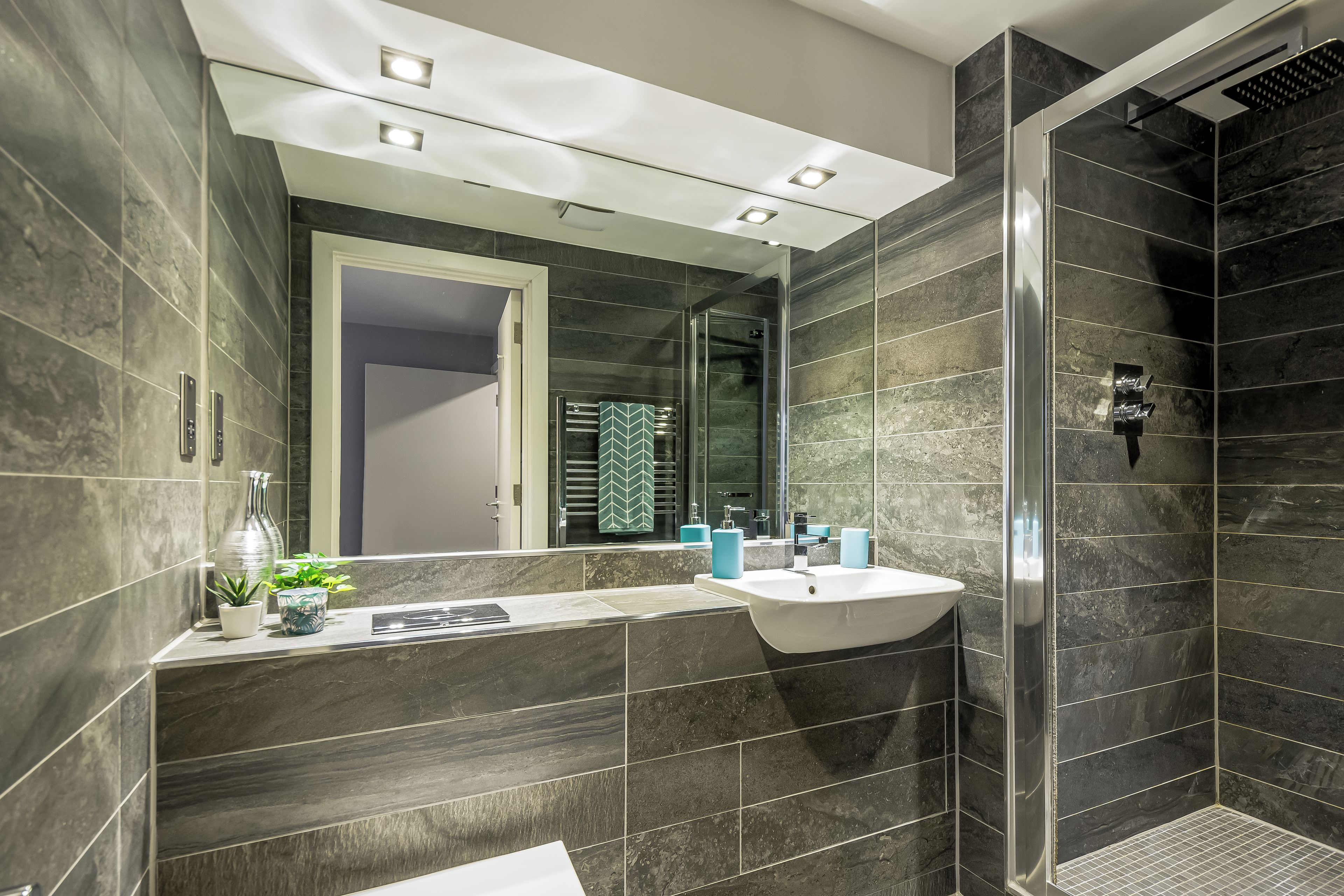 Un baño moderno con un espejo grande, un lavabo y una zona de ducha.