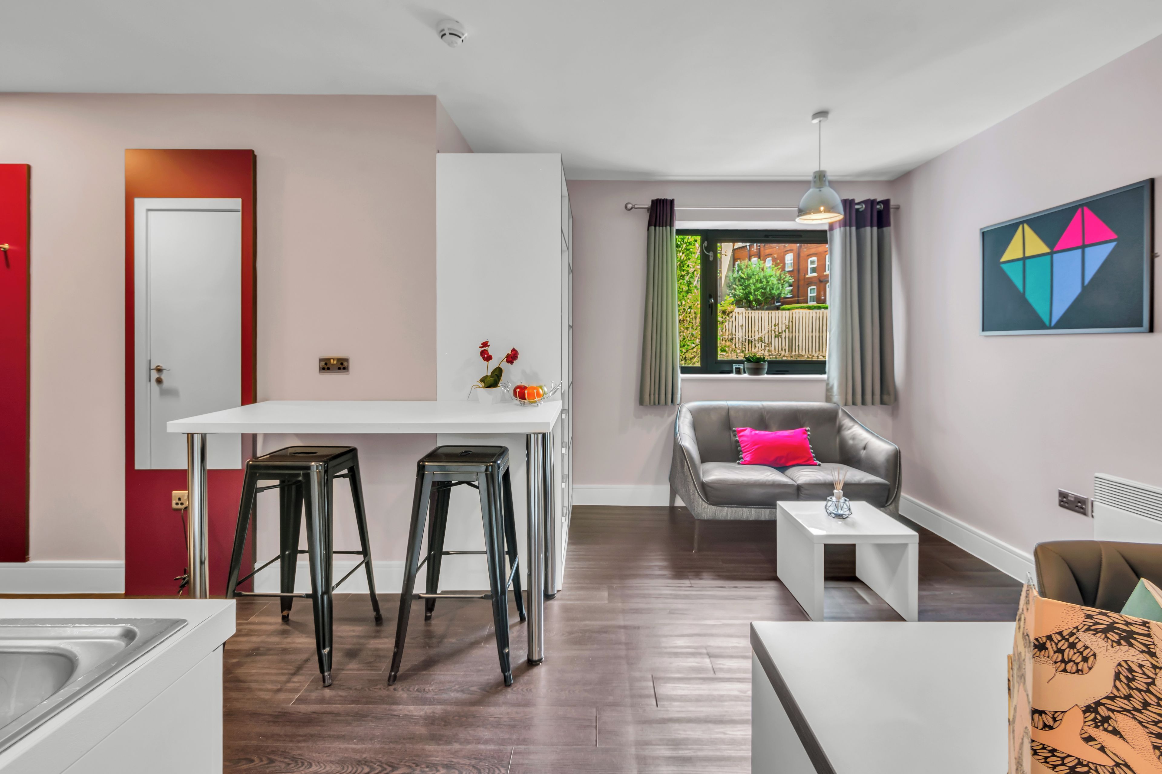 A modern kitchen with a white countertop, two black stools, and a window with curtains.