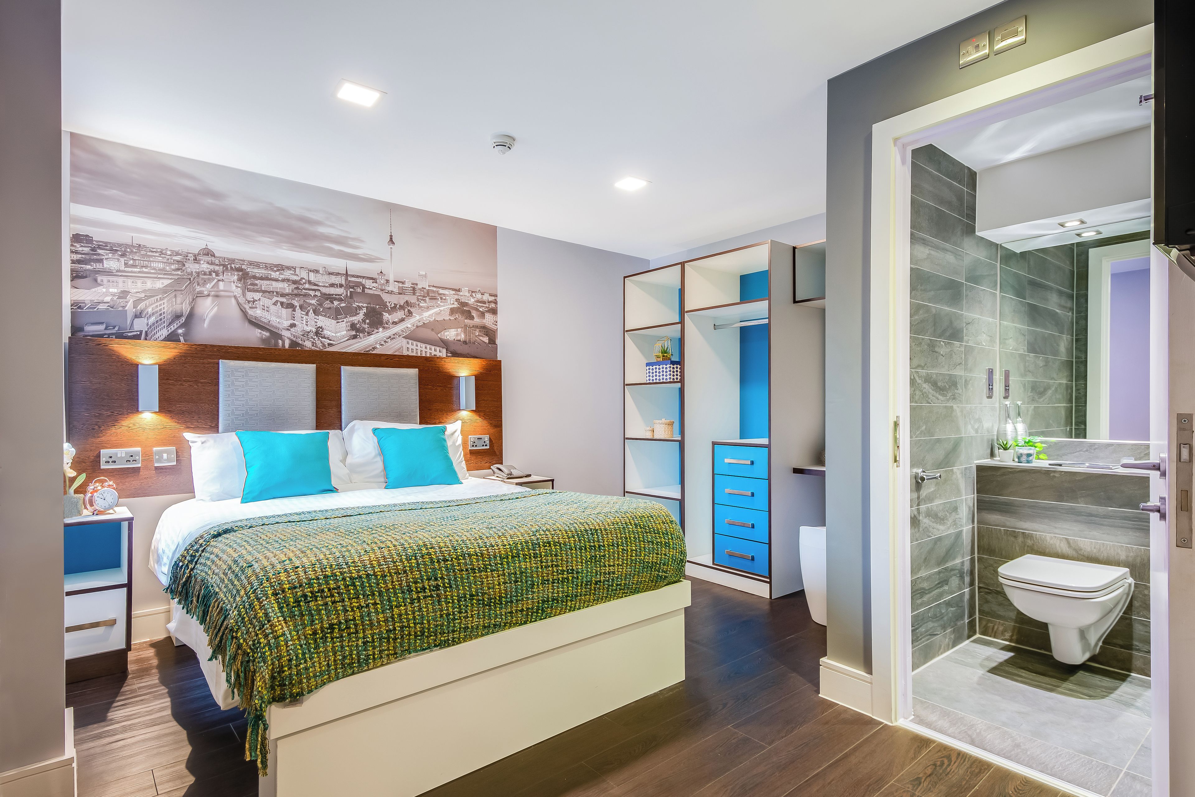 Una habitación de hotel moderna con una cama grande, un mural de la ciudad, un vestidor y un baño separado.