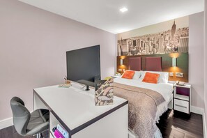 A modern hotel room with a desk, chair, bed, and a cityscape mural on the wall. - Roomzzz The Edge (Leeds)