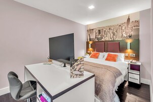 A modern hotel room with a desk, chair, bed, and a cityscape mural on the wall.