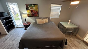 Quarto com cama, escrivaninha, cadeira, abajur, quadro e janela com persianas.