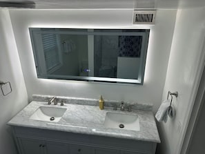 Une salle de bain avec un meuble-lavabo à deux vasques, un grand miroir et un porte-serviettes.