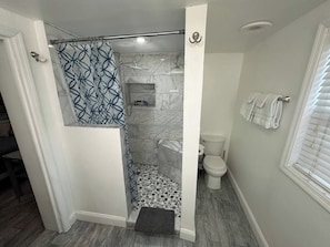 Casa de banho com chuveiro, sanita e porta-toalhas.