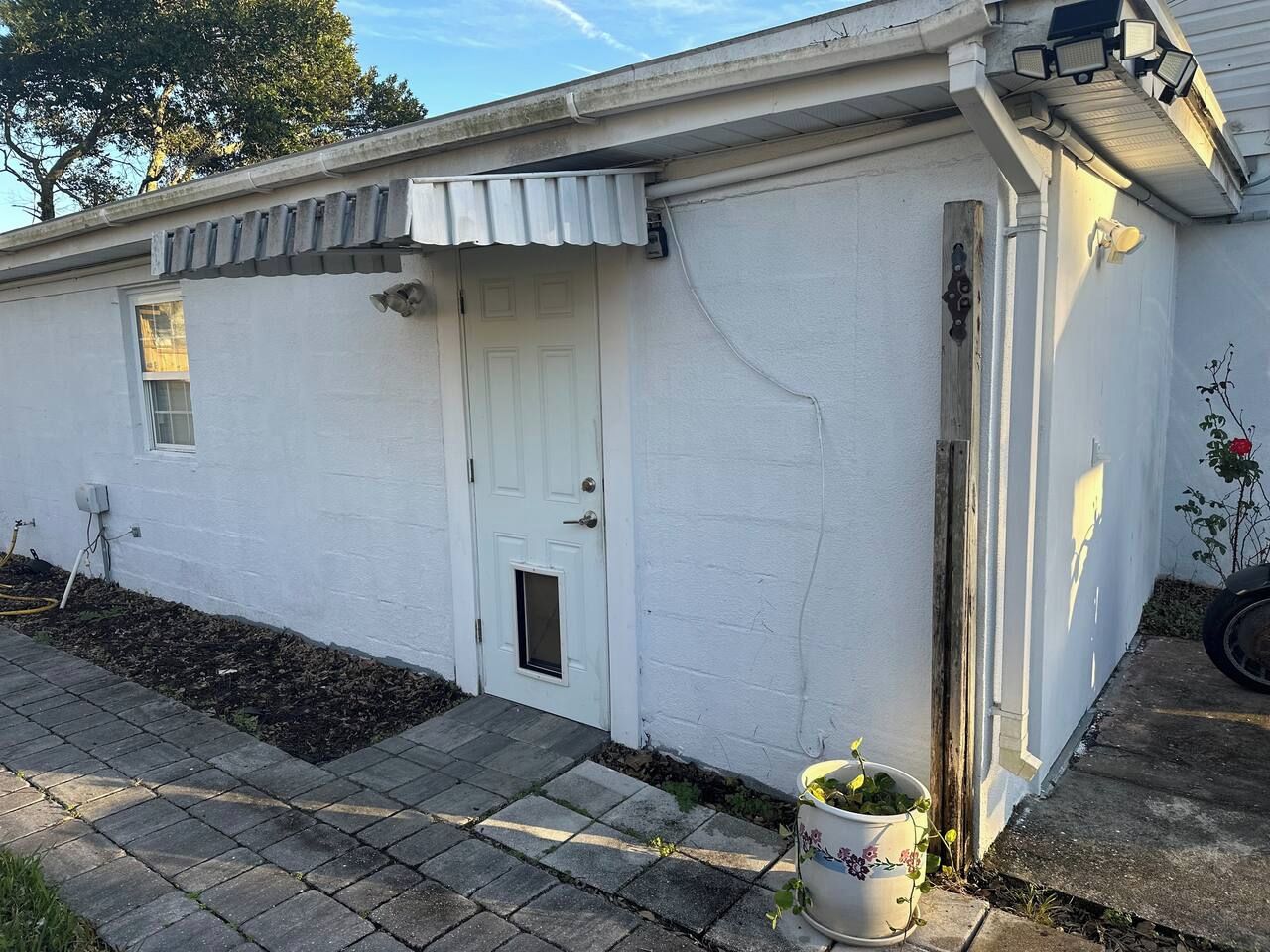 Um edifício branco com uma porta, uma pequena janela e uma planta em vaso.