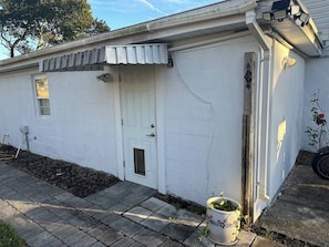 Um edifício branco com uma porta, uma pequena janela e uma planta em vaso.