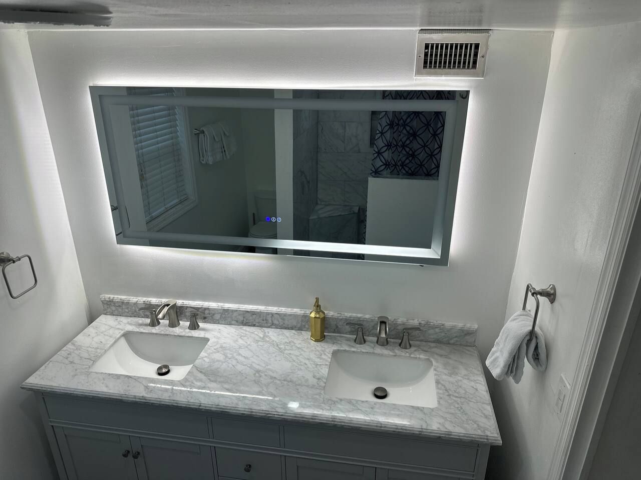 A bathroom with a double sink vanity, a large mirror, and a towel rack.