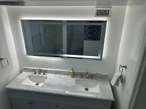 Casa de banho com lavatório duplo, espelho grande e porta-toalhas.