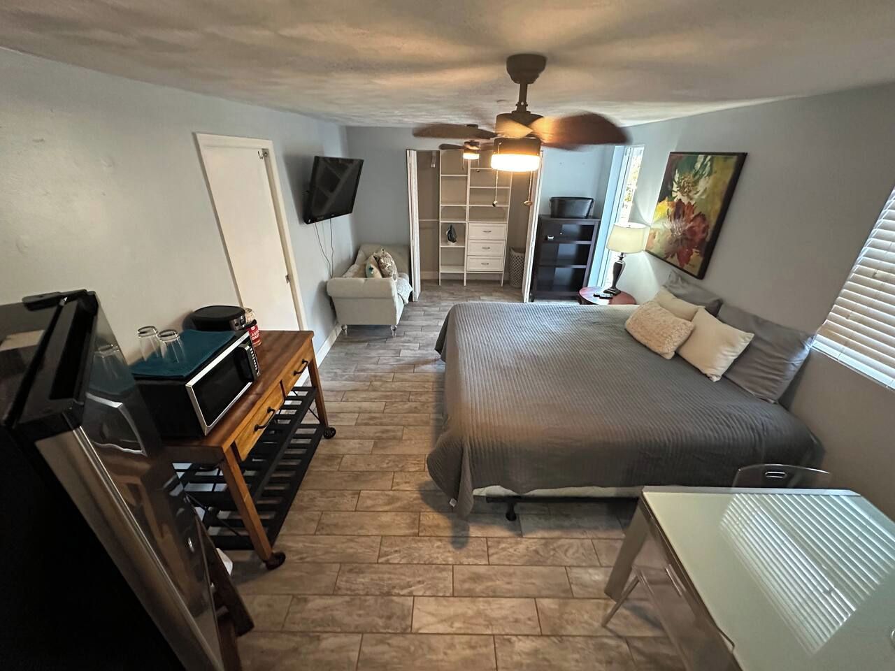 A bedroom with a bed, a desk, a chair, a ceiling fan, a TV, and a wardrobe.