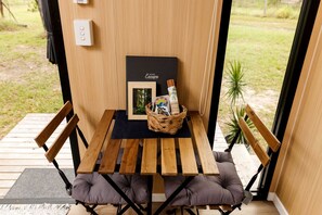 Ein Holztisch mit einer schwarzen Matte, zwei gepolsterte Stühle, ein Korb mit Gegenständen und ein gerahmtes Buch mit dem Titel 'Escape' an der Wand.