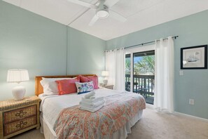 Ein Schlafzimmer mit einem Bett, zwei Nachttischen, einem Deckenventilator, einem Fenster mit Vorhängen und einem gerahmten Bild an der Wand.
