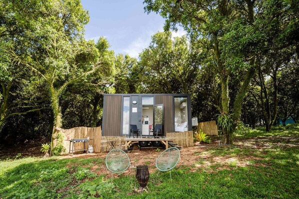 Una cabaña moderna y compacta con terraza, rodeada por un bosque denso.