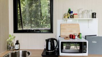 A compact kitchen with a window, a microwave, a kettle, and a sink.