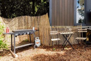 Un área de barbacoa al aire libre con una parrilla, un tanque de gas y una mesa con sillas.