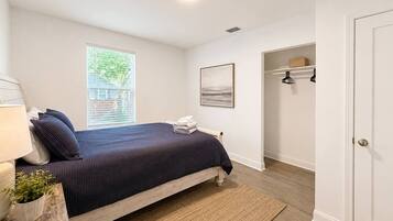 A bedroom with a bed, a bedside table with a lamp, a window, and a door.