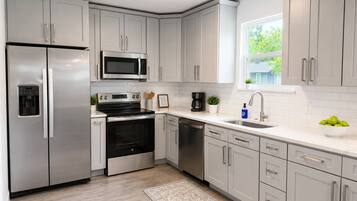 A modern kitchen with stainless steel appliances, white cabinetry, and a window providing natural light.
