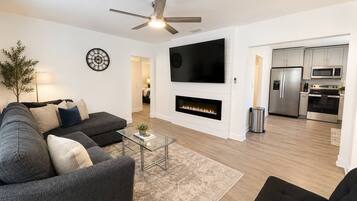 A modern living room with a fireplace, a flat-screen TV, and a ceiling fan.