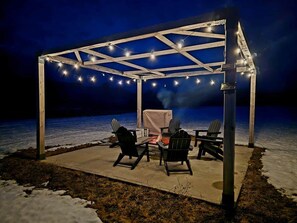 Eine Terrassenanlage im Freien mit einer Pergola, Lichterketten und einem Grill.