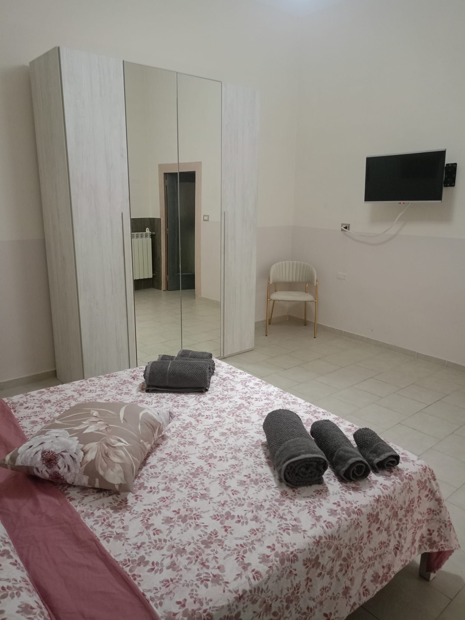 Une chambre à coucher comprenant un lit, une armoire, une chaise et un téléviseur fixé au mur.
