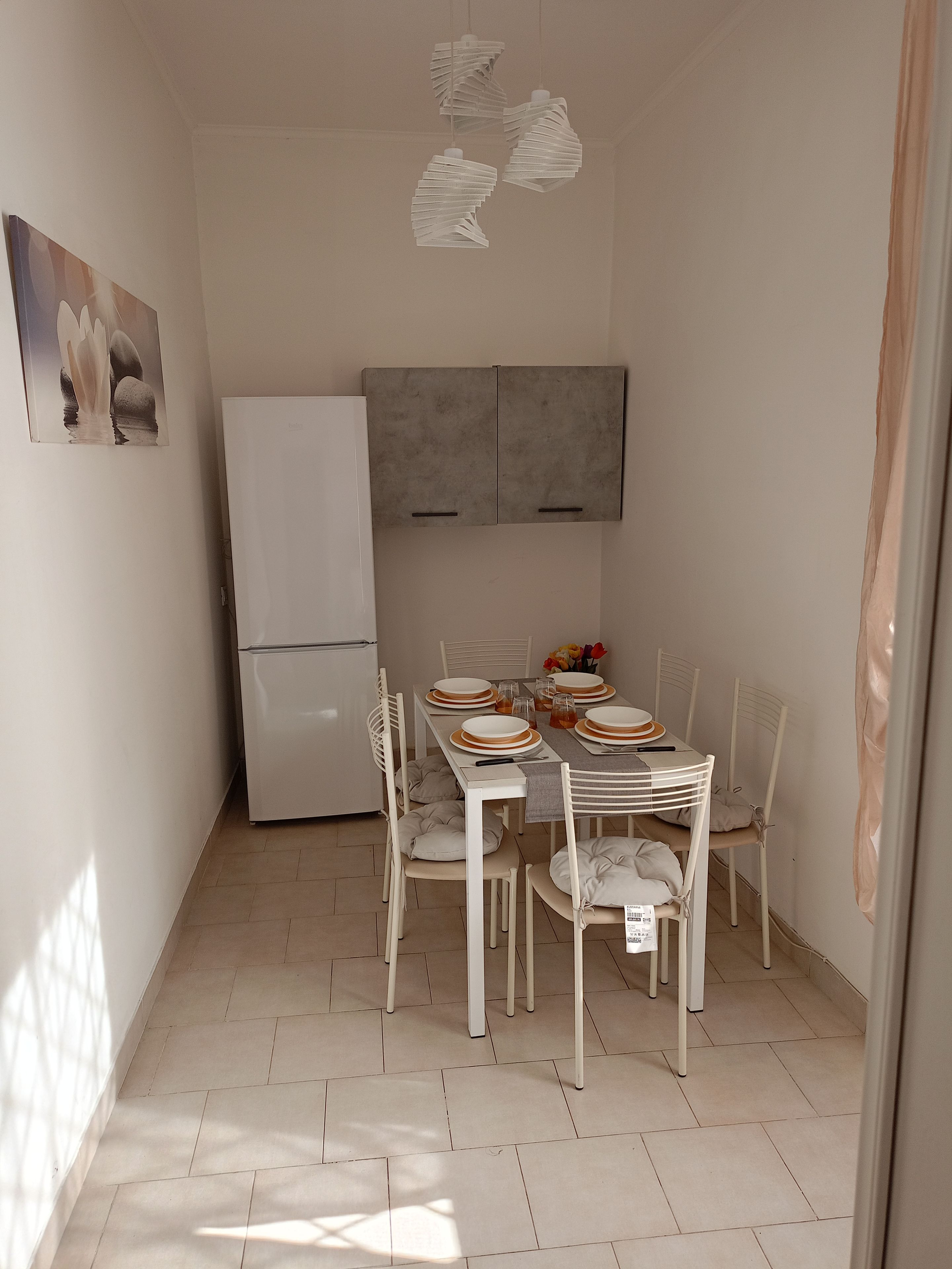 Un petit coin repas avec une table blanche dressée pour quatre personnes, un réfrigérateur blanc et un meuble gris placé au-dessus.