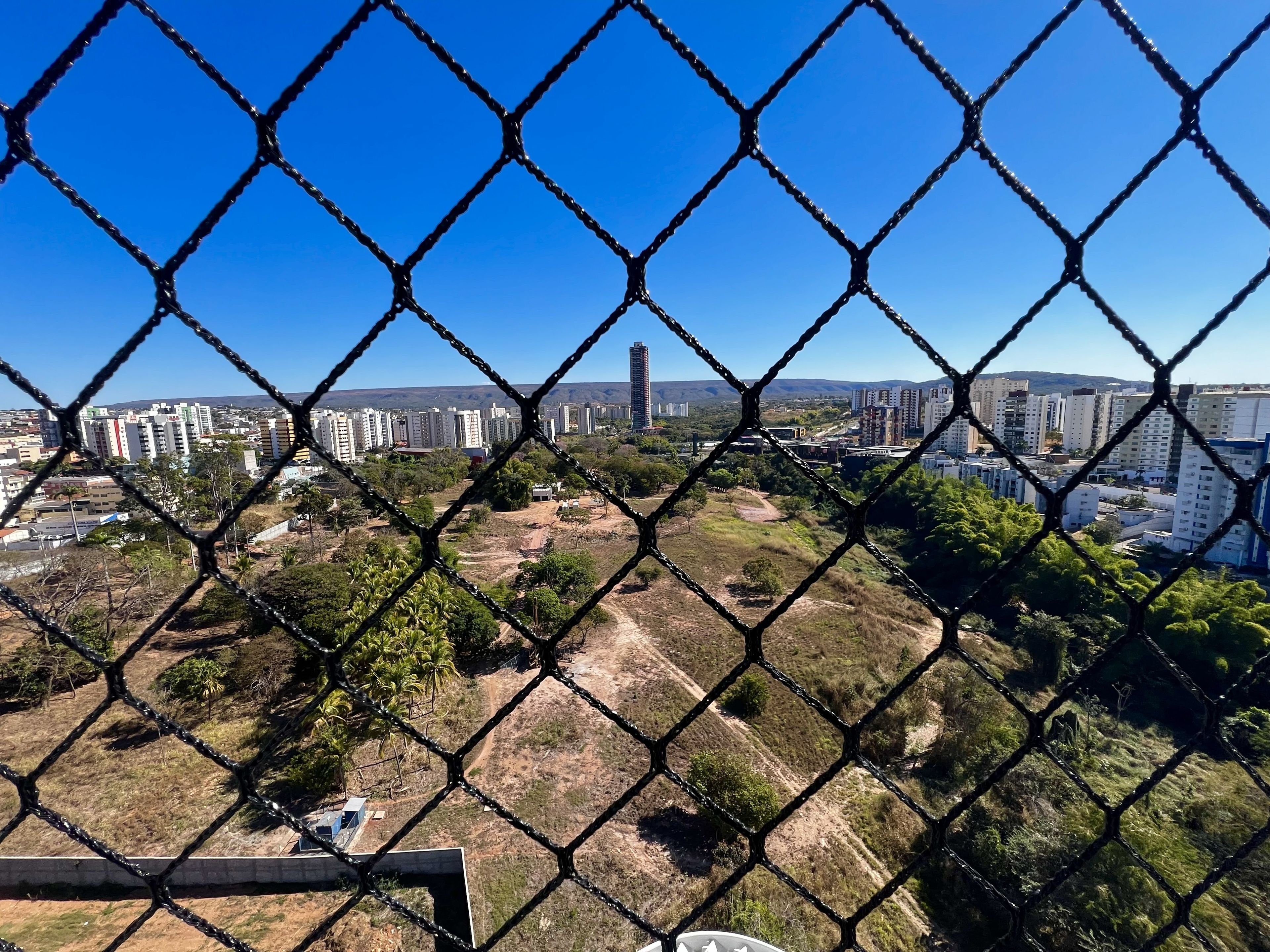 A chain-link fence with a view of a cityscape, including buildings and a hill in the background.