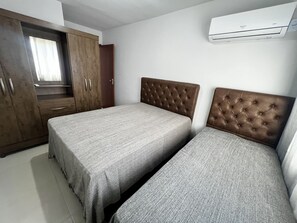 A bedroom with two beds, a wardrobe, and an air conditioning unit.