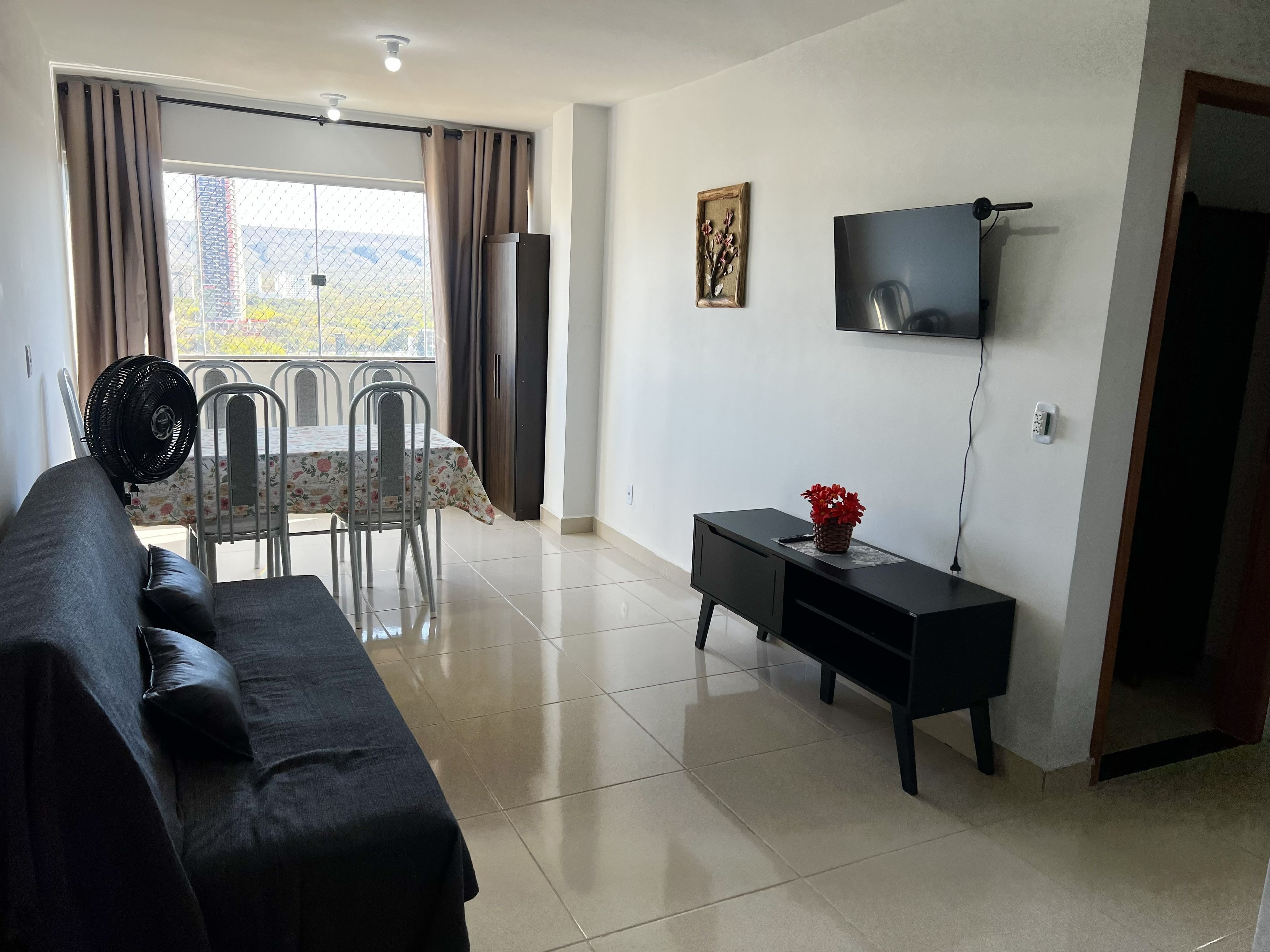 A living room with a sofa, a dining table with chairs, a TV, and a small console table with a plant.