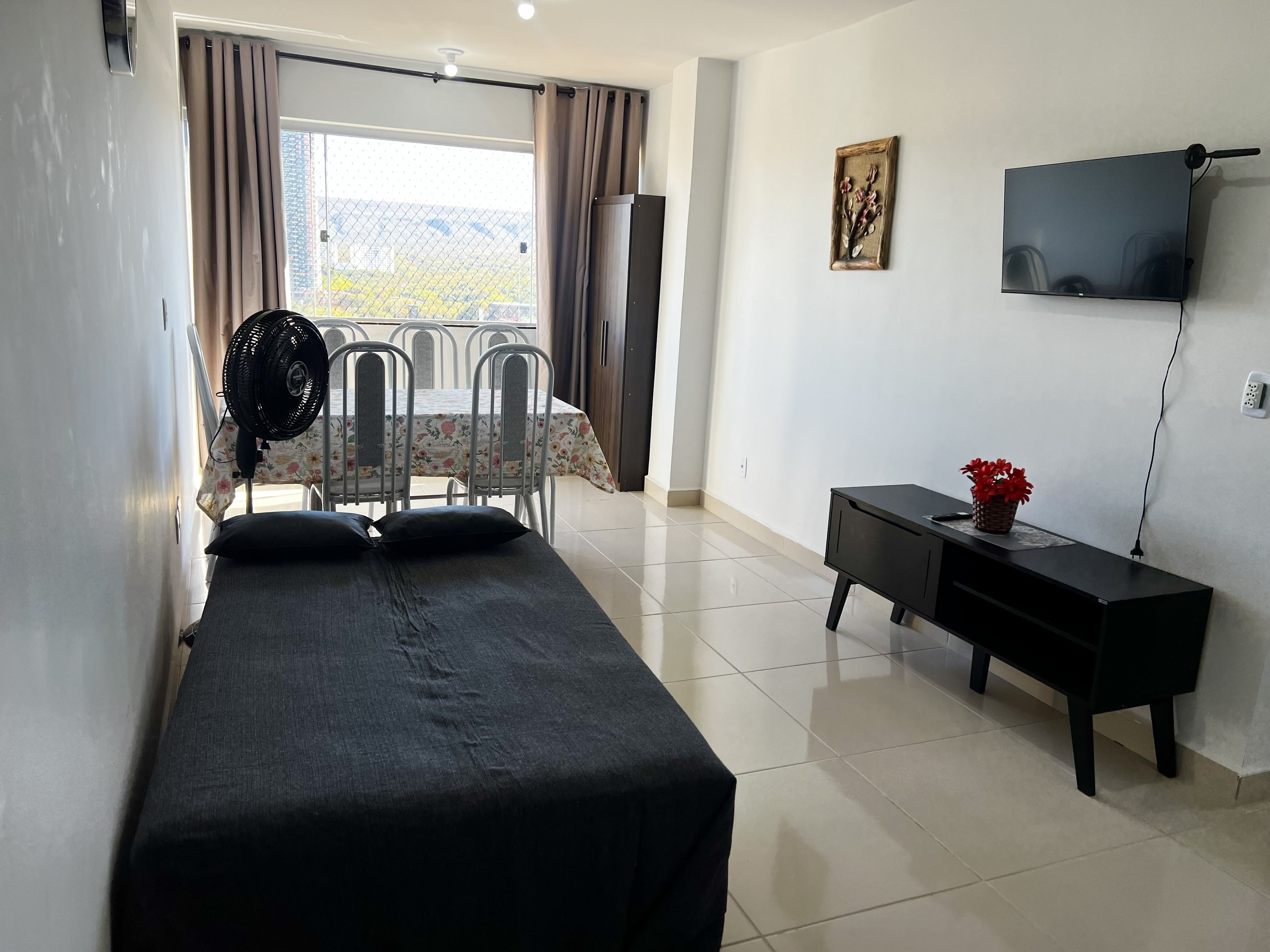 A hotel room with a bed, a desk, a TV, and a balcony with a fan.