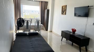 A hotel room with a bed, a desk, a TV, and a balcony with a fan.