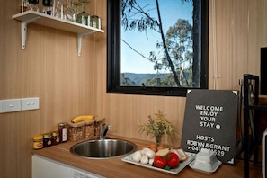 A kitchen with a view of trees and hills, a welcome sign, and various food items on the counter.