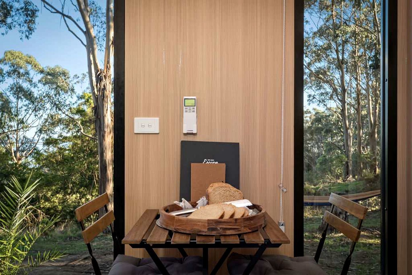 Ein Zimmer mit einem Holztisch, zwei Stühlen, einer Bank, einem kleinen Tisch mit Brot und einem Thermostat an der Wand.