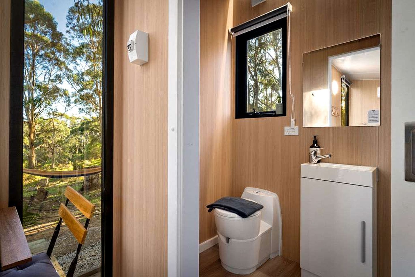 A compact bathroom with a toilet, sink, and a window with a view of trees.