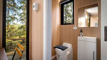 A compact bathroom with a toilet, sink, and a window with a view of trees.