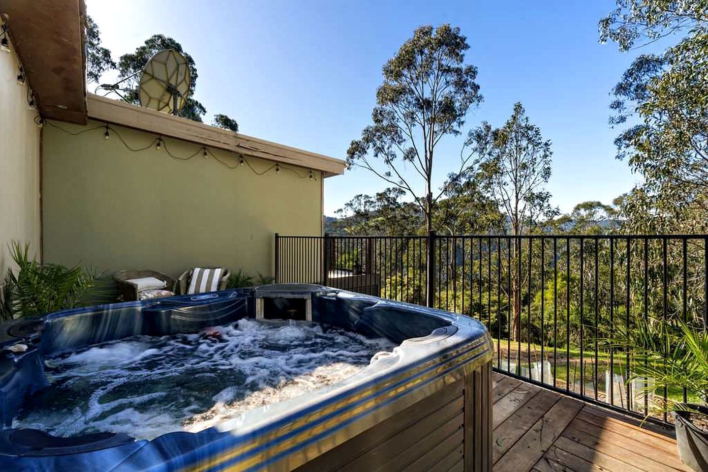 Een hottub op een houten terras met uitzicht op bomen en een hek.