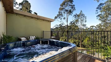 Een hottub op een houten terras met uitzicht op bomen en een hek.