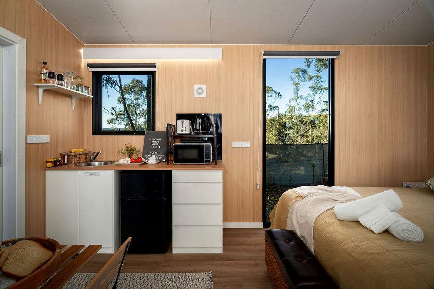 A compact room with a kitchenette, a bed, and a view of the outdoors.