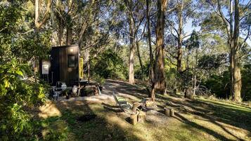 A rustic cabin with a fire pit, surrounded by dense forest.