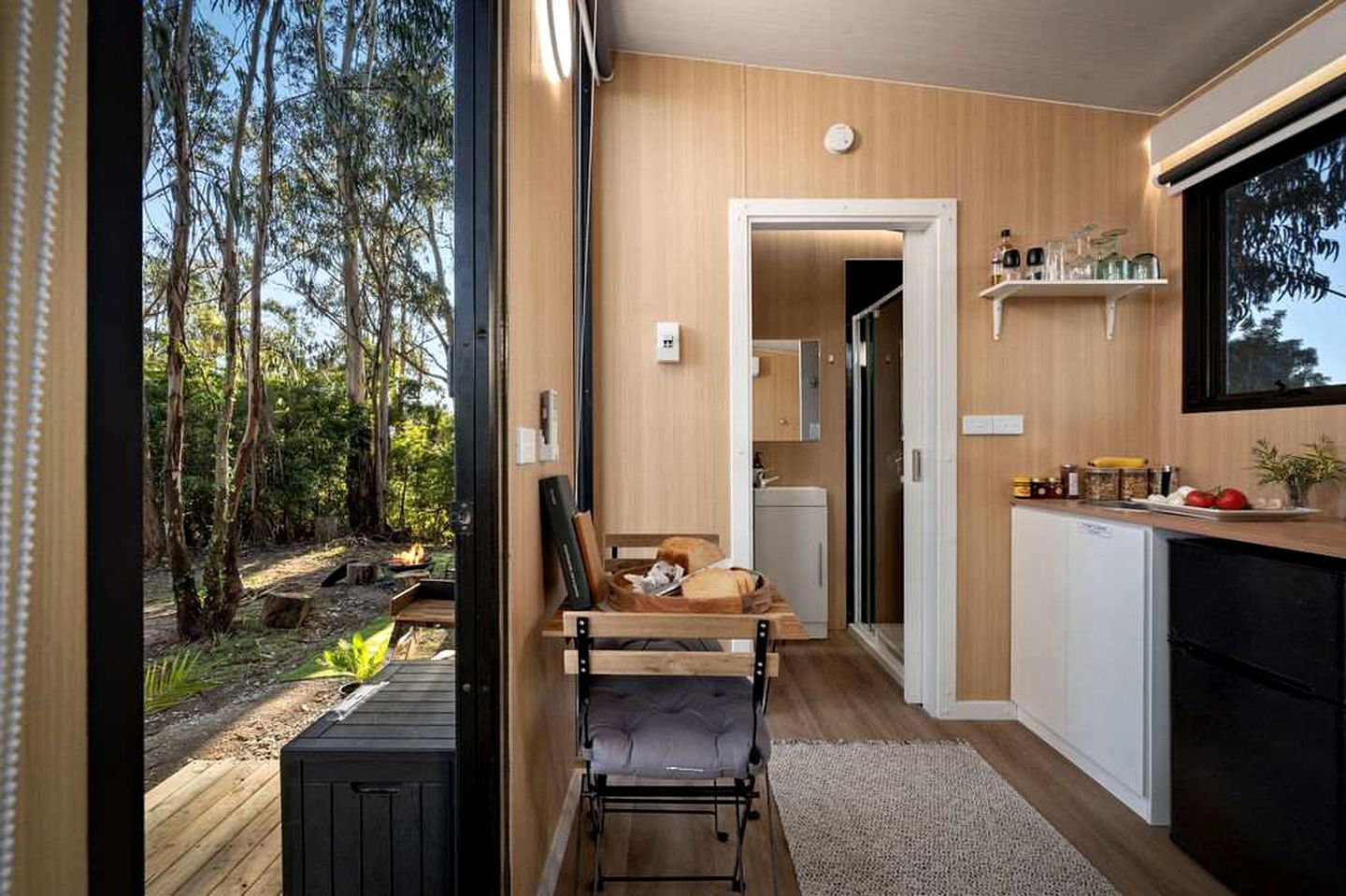 Une cuisine moderne avec des meubles en bois, un coin repas avec un banc et une vue sur l’extérieur.