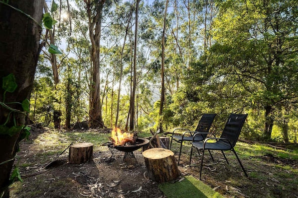 A campsite with a fire pit, two chairs, and a natural forest setting.