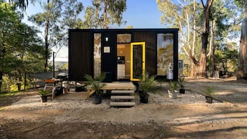 A compact cabin with a dark exterior, a wooden deck, and a clear door.