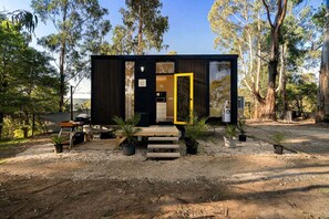 A compact cabin with a dark exterior, a wooden deck, and a clear door.