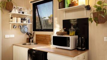 A compact kitchen with a microwave, sink, and a window overlooking a forest.