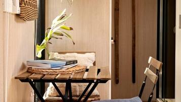 A compact room with a wooden floor, a folding table with a plant, a chair, and a wall-mounted shelf with a woven bag.
