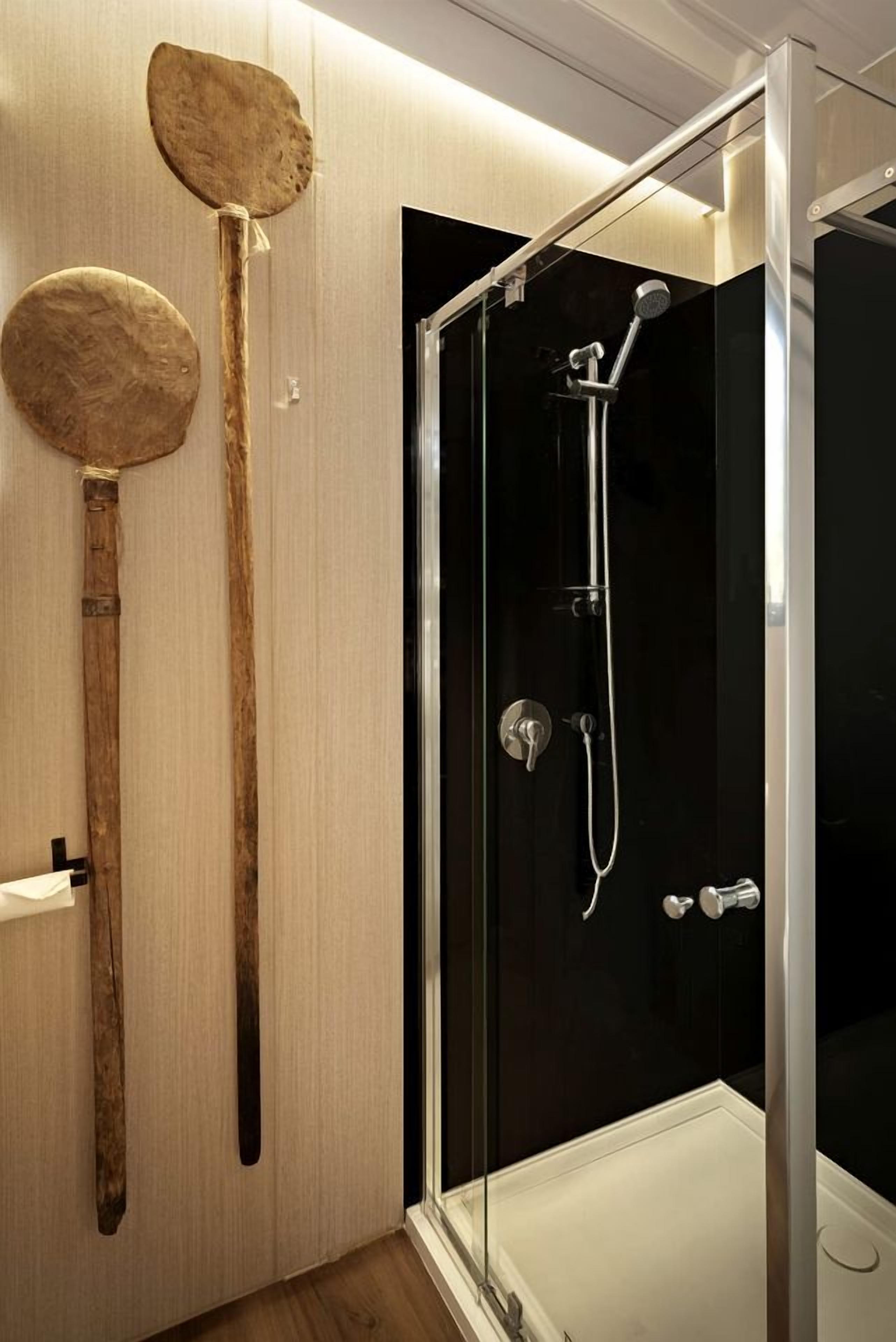 Un baño moderno con ducha de vidrio, utensilios de madera colgados en la pared y un toallero blanco.
