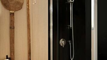 Un baño moderno con ducha de vidrio, utensilios de madera colgados en la pared y un toallero blanco.
