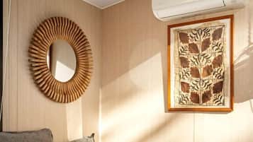 Un dormitorio con cama, almohadas, un espejo circular y una obra de arte enmarcada en la pared.