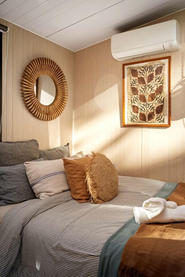 A bedroom with a bed, pillows, a circular mirror, and a framed artwork on the wall.