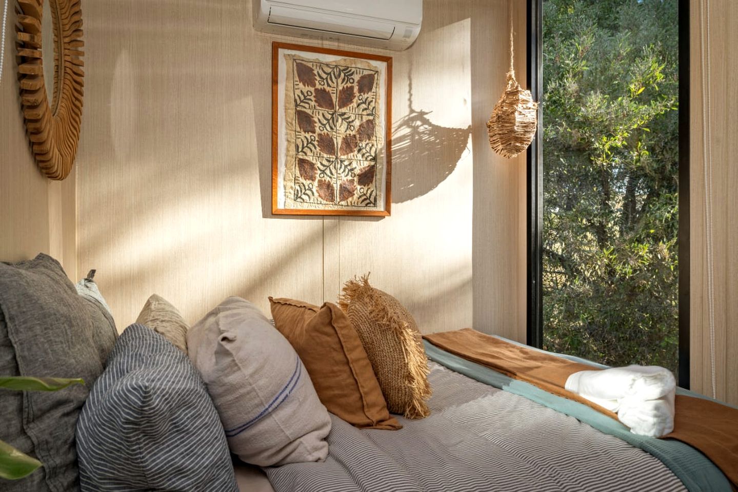 A cozy room with a bed, pillows, a framed artwork, and a hanging light fixture.
