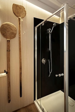 A modern bathroom with a glass-enclosed shower, wooden utensils hanging on the wall, and a white towel rack.