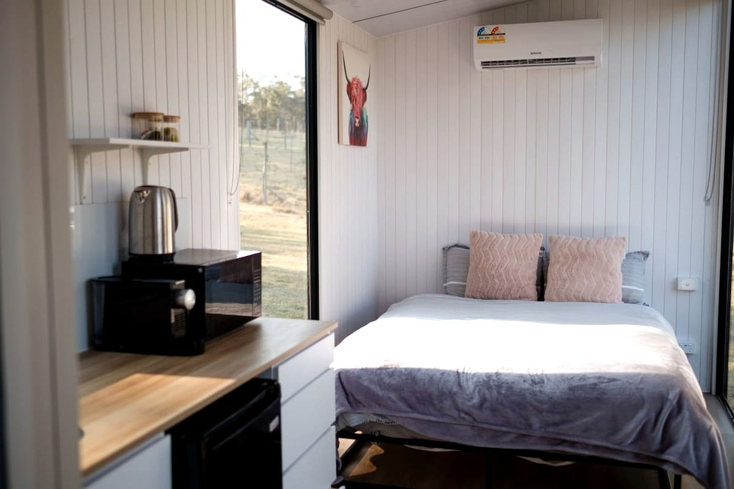 Een slaapkamer met een bed, kussens, een koffiezetapparaat en een raam.